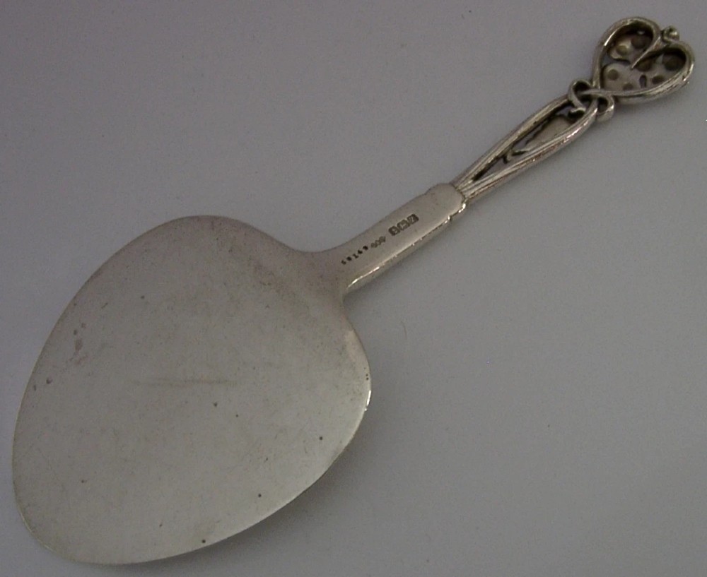 A sterling silver pastry server with a rounded flat spade blade and an openwork handle decorated with carved leaf and grape cluster motifs. View VII