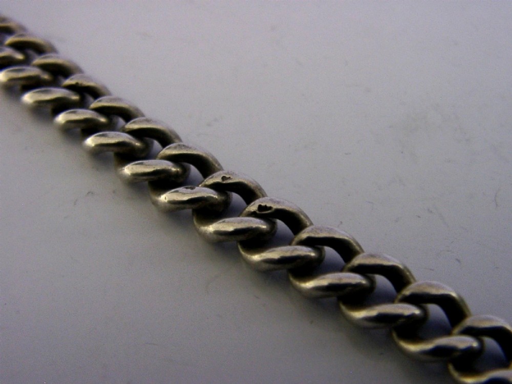 An Edwardian sterling silver curb-link pocket watch chain featuring a T-bar, swivel clip, and an engraved dome-shaped seal fob. View X