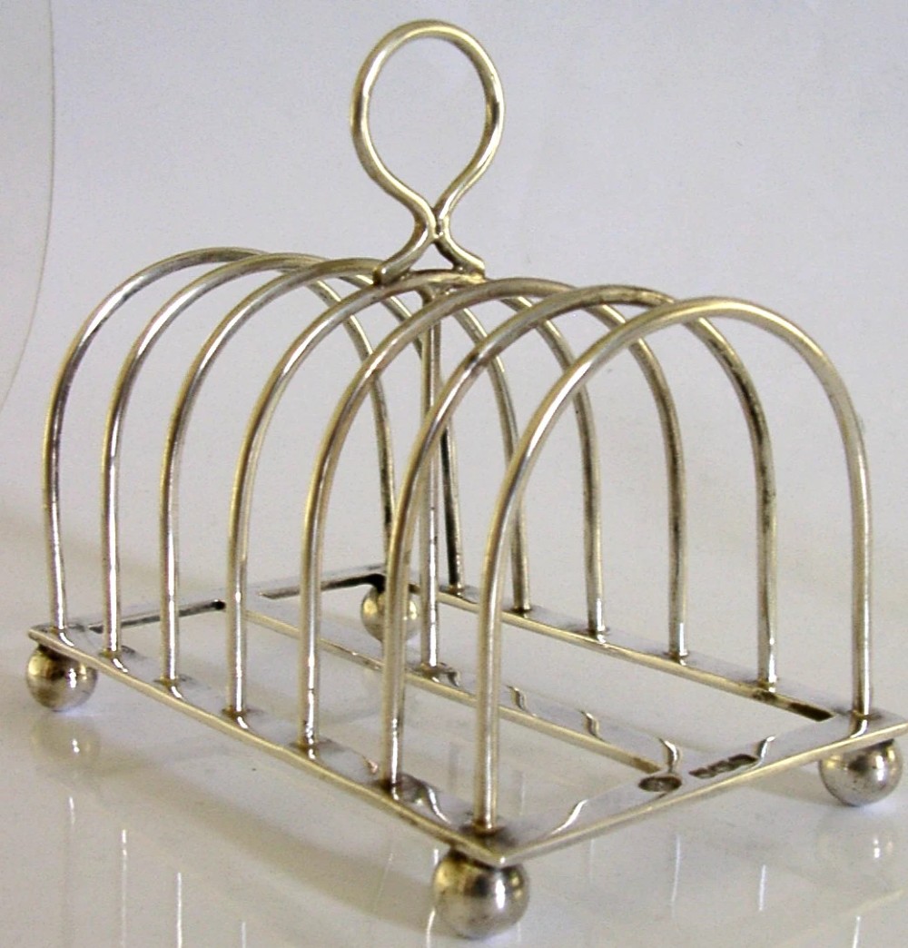 A sterling silver six-slice toast rack featuring seven arched wire divisions, a central loop handle, and four ball feet resting on a rectangular base. View III