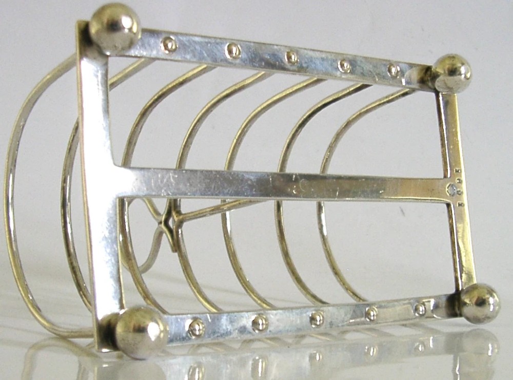A sterling silver six-slice toast rack featuring seven arched wire divisions, a central loop handle, and four ball feet resting on a rectangular base. View VII