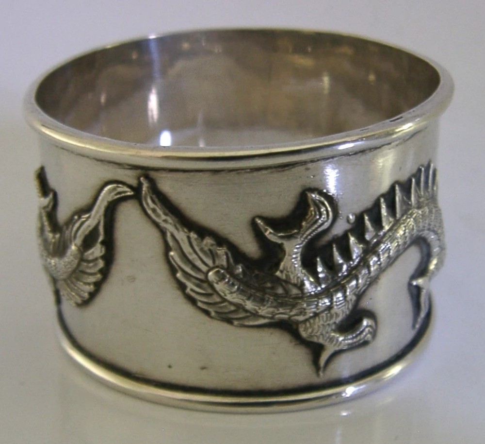 A cylindrical silver napkin ring featuring a relief-carved Chinese dragon motif against a polished surface. View V