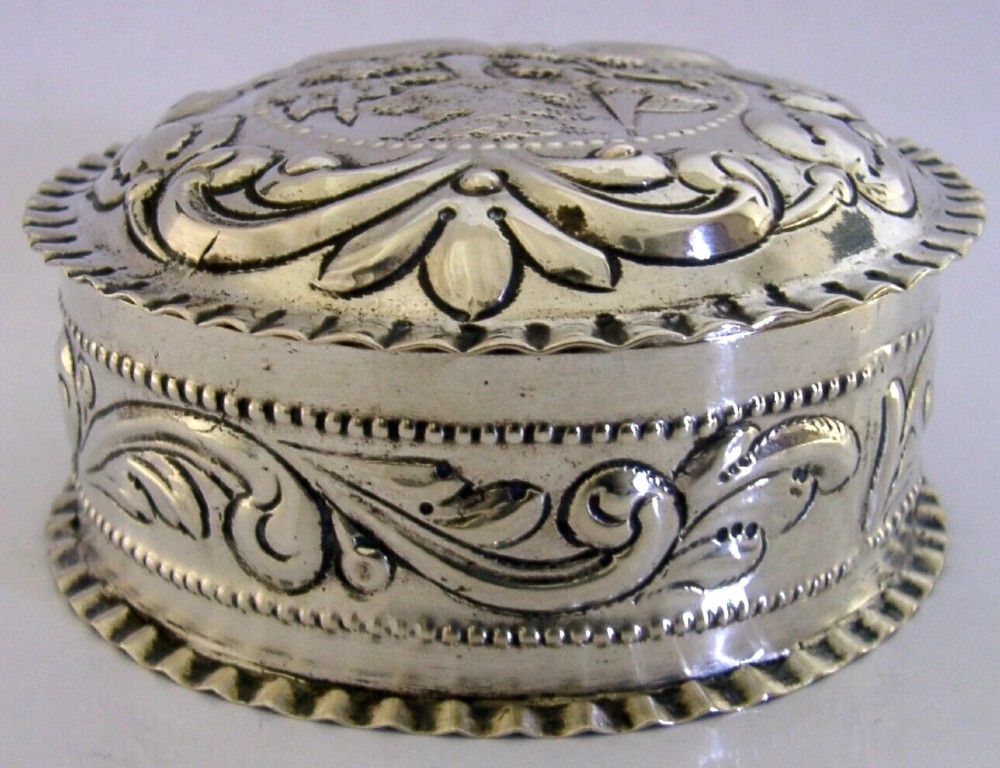A circular solid silver table box featuring embossed repousse detail of a castle scene framed by acanthus scrolls and fluted edges. View VIII