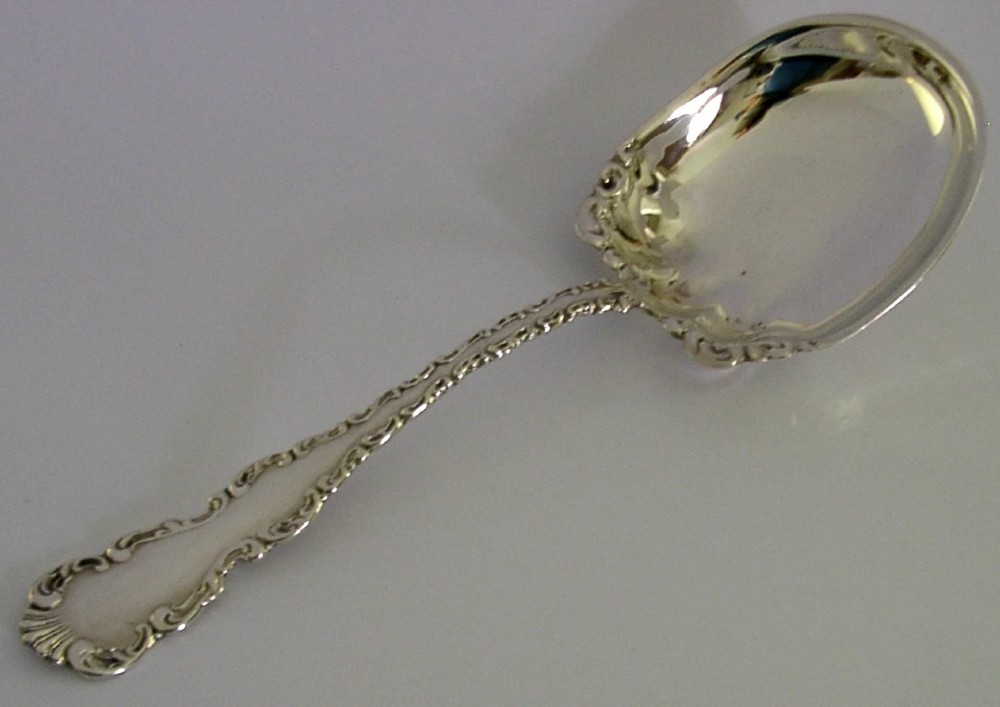 An antique sterling silver serving spoon featuring a scalloped shell-shaped bowl and an ornate scrollwork handle. View III