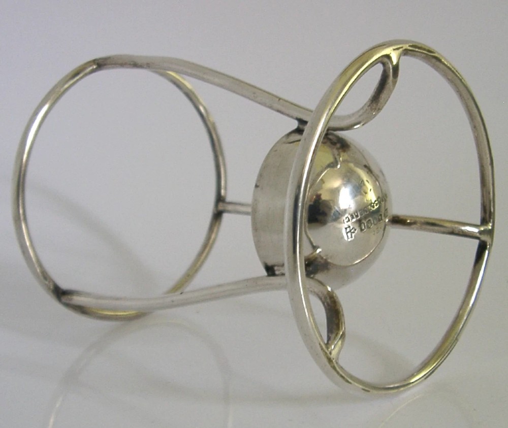 A Victorian silver-plated wirework stand designed to hold a Hamilton torpedo bottle, featuring a circular base, curved uprights, a top ring, and a central cup. View IV
