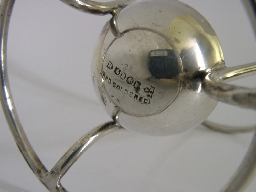 A Victorian silver-plated wirework stand designed to hold a Hamilton torpedo bottle, featuring a circular base, curved uprights, a top ring, and a central cup. View VI