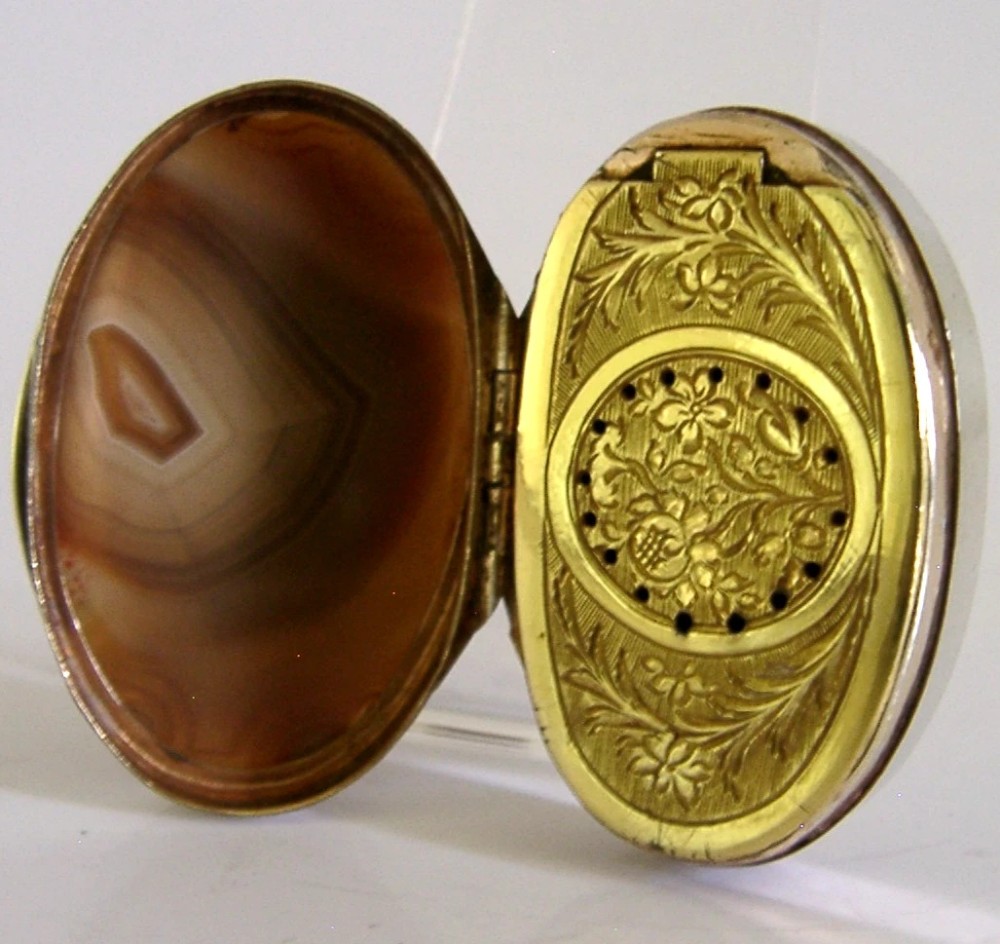 An open Georgian silver oval vinaigrette box featuring a translucent banded agate lid insert and a perforated gold-gilded floral inner grille. View VI