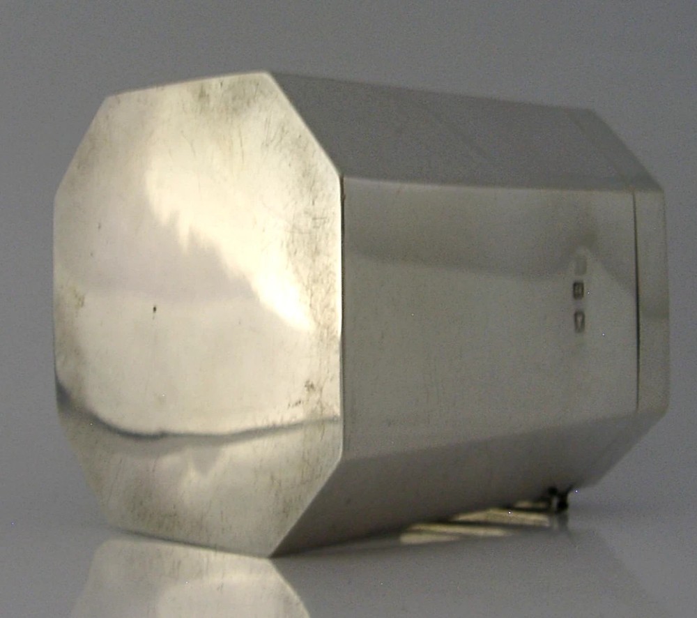 An octagonal sterling silver tea caddy featuring a faceted domed lid, scroll finial, and British hallmarks stamped near the rim. View IX