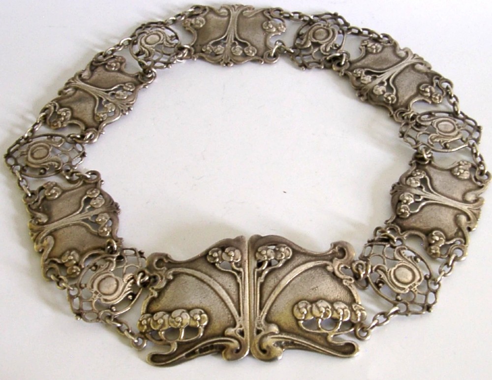 An antique Art Nouveau sterling silver linked waist belt featuring intricate floral panels and a central interlocking buckle.