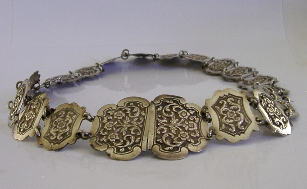 An antique Indian silver belt featuring intricate floral chased link panels and a matching central buckle.