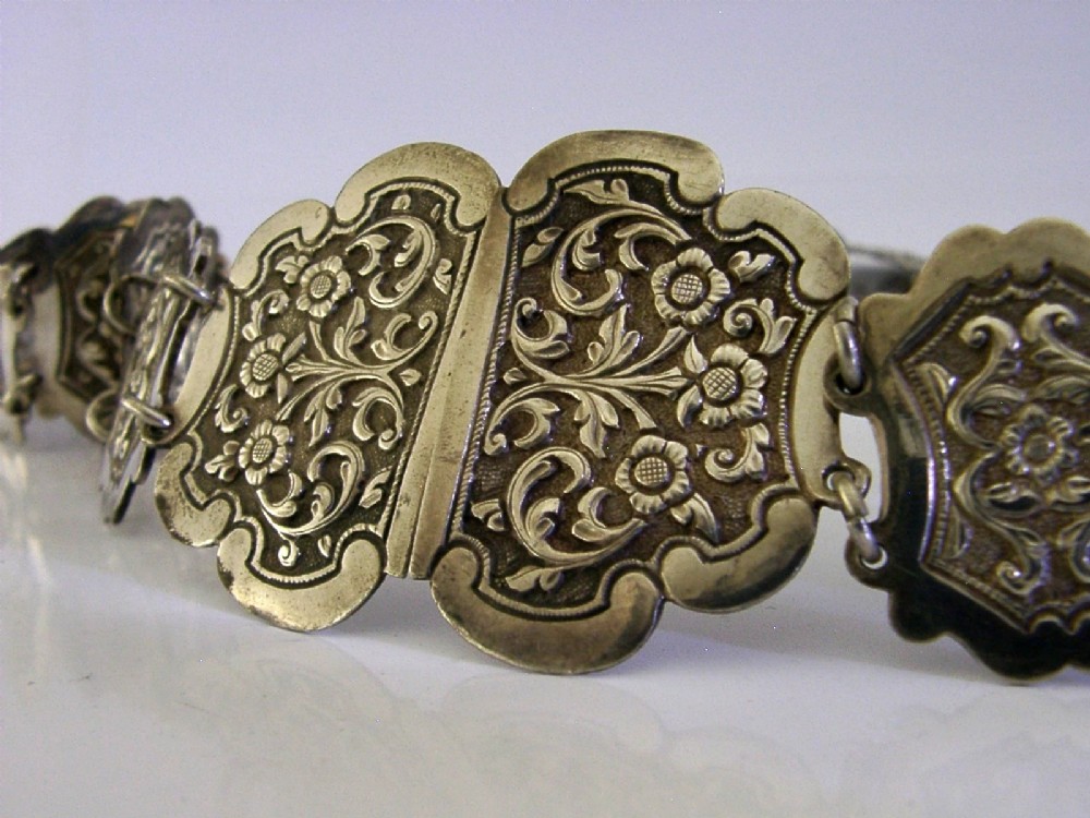 An antique Indian silver belt featuring intricate floral chased link panels and a matching central buckle. View II