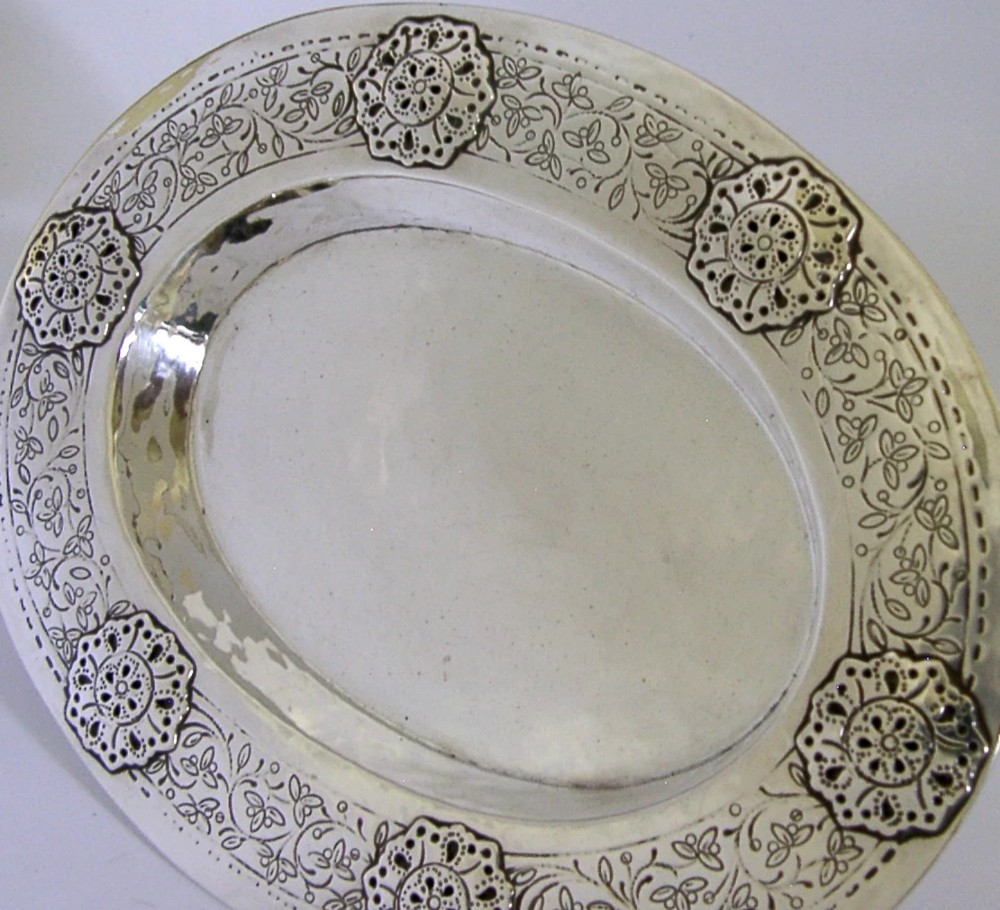 An oval antique sterling silver dish featuring a planished centre and a wide rim decorated with chased floral rosettes and leaf motifs. View II