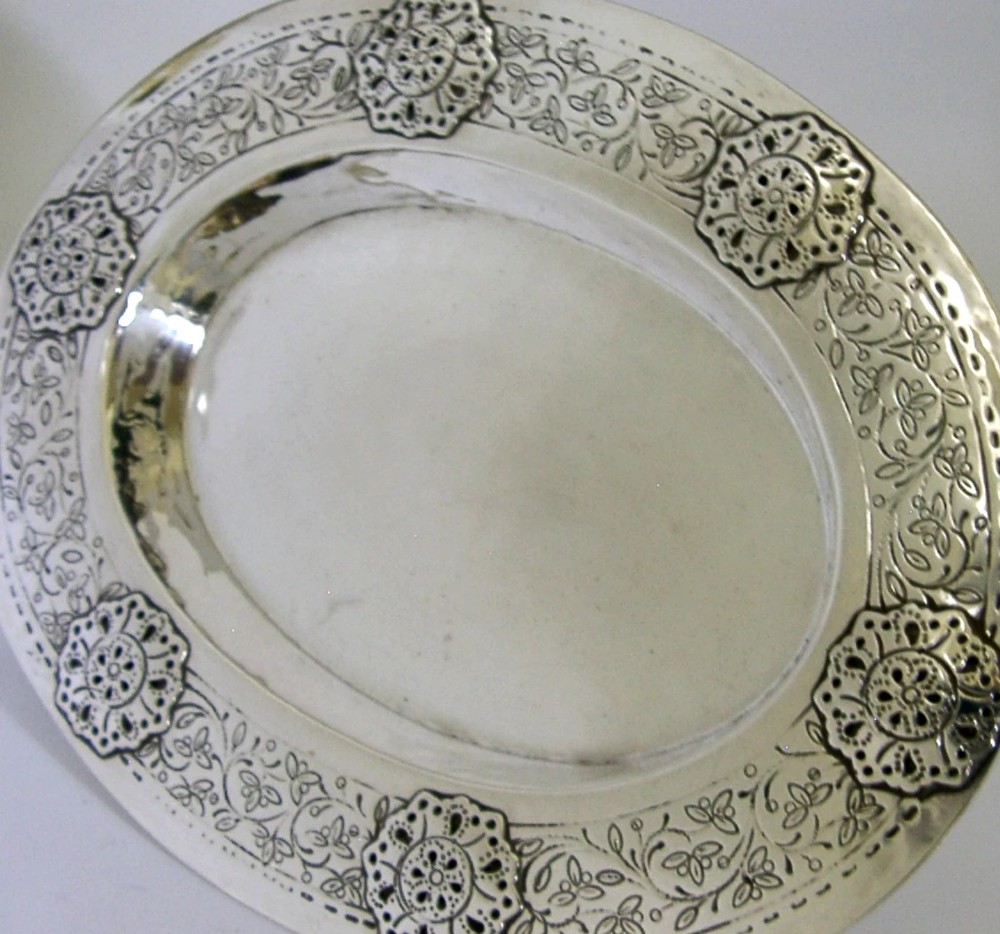 An oval antique sterling silver dish featuring a planished centre and a wide rim decorated with chased floral rosettes and leaf motifs. View III