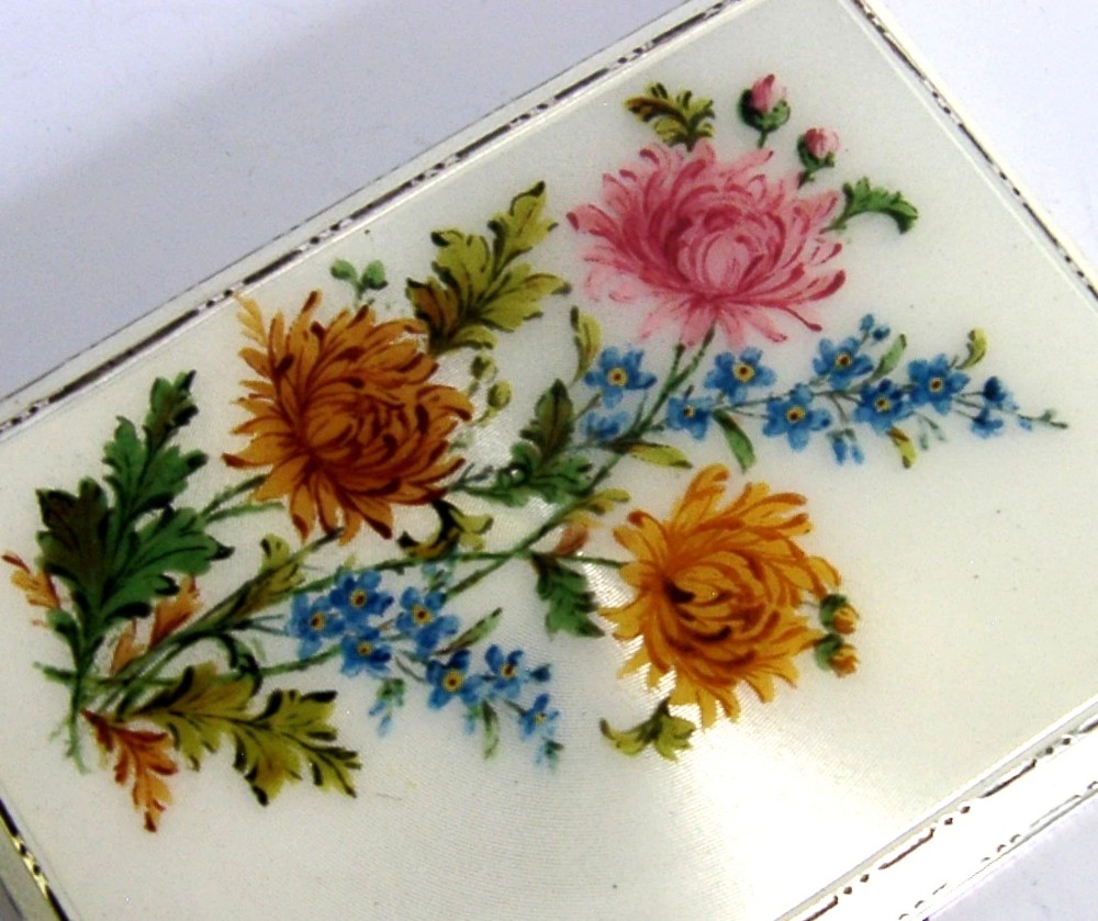 A square sterling silver hinged cigarette case showing an engine-turned textured exterior on one side and a white enamelled panel with hand-painted yellow and pink chrysanthemums on the other. View II