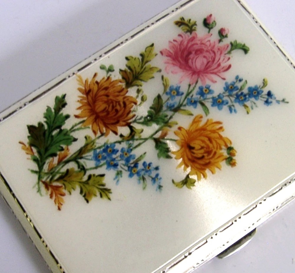 A square sterling silver hinged cigarette case showing an engine-turned textured exterior on one side and a white enamelled panel with hand-painted yellow and pink chrysanthemums on the other. View III