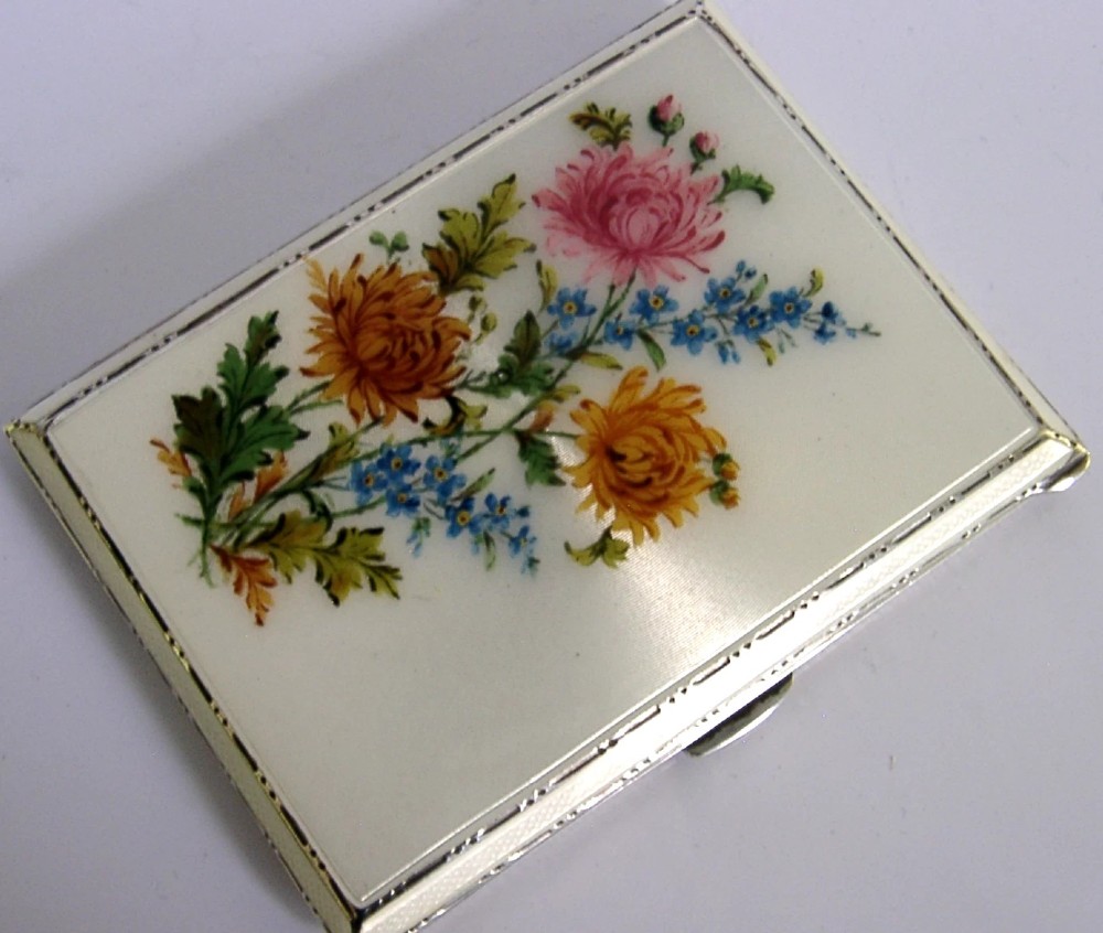 A square sterling silver hinged cigarette case showing an engine-turned textured exterior on one side and a white enamelled panel with hand-painted yellow and pink chrysanthemums on the other. View VI