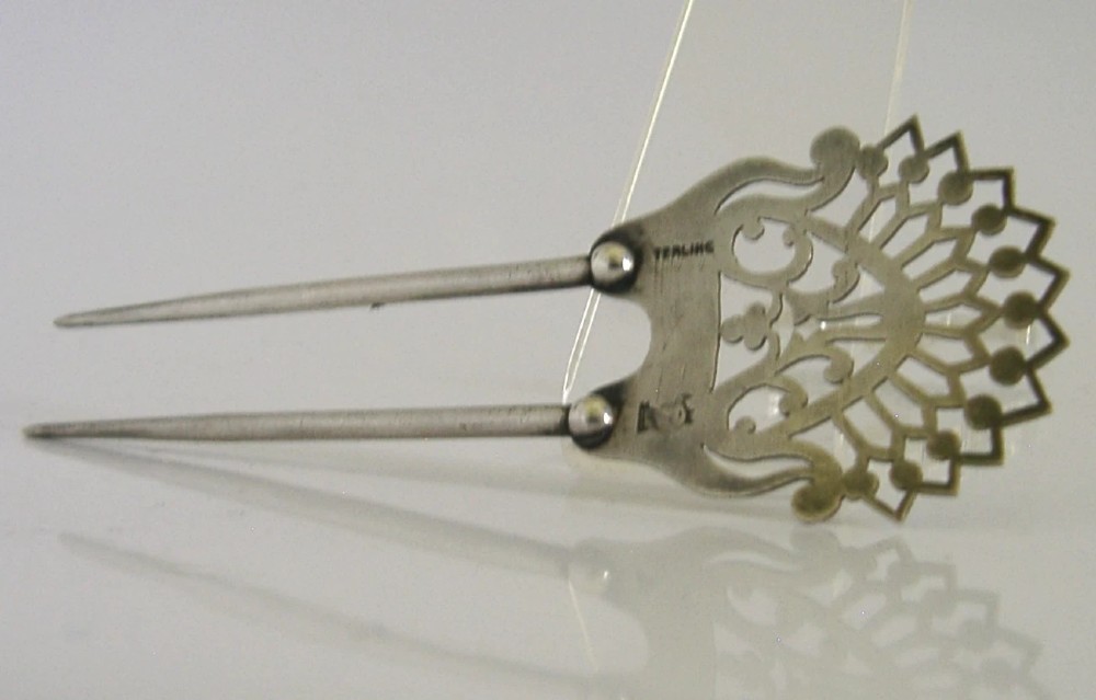 An antique sterling silver two-prong hair slide featuring a fan-shaped pierced crest with scrolling motifs and geometric openwork. View VIII