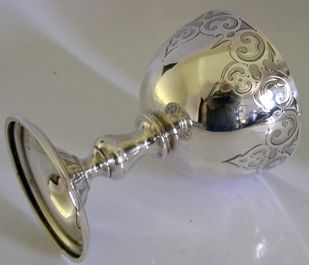 A mid-Victorian sterling silver chalice featuring an engraved scroll pattern around the cup, a central knopped stem, and a leaf-patterned circular base. View VI