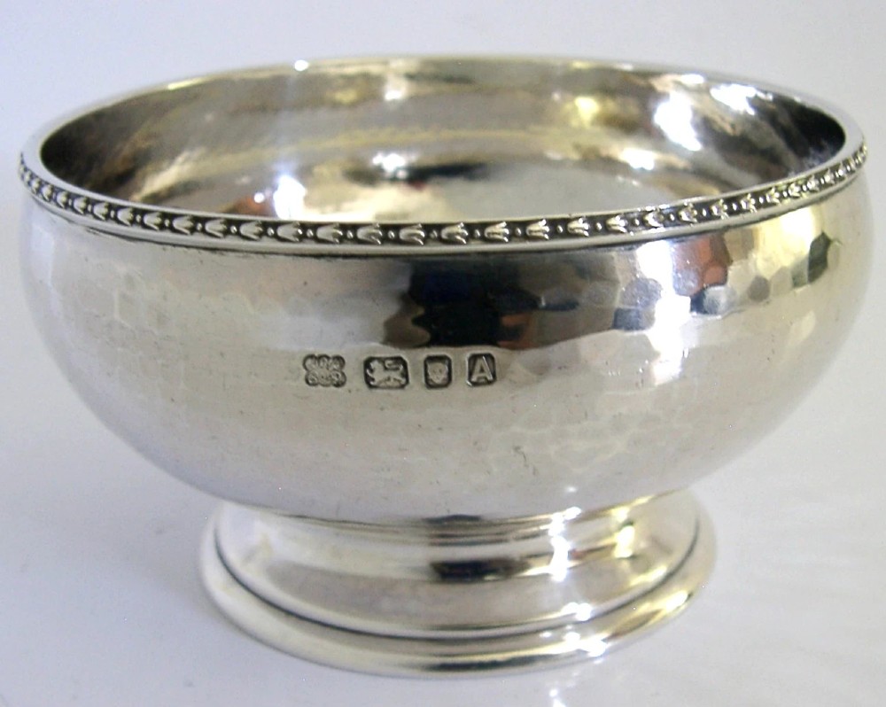 A planished sterling silver bowl featuring a hand-hammered finish, patterned rim, pedestal base, and British hallmarks stamped on the side.