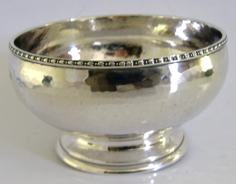 A planished sterling silver bowl featuring a hand-hammered finish, patterned rim, pedestal base, and British hallmarks stamped on the side. View IV