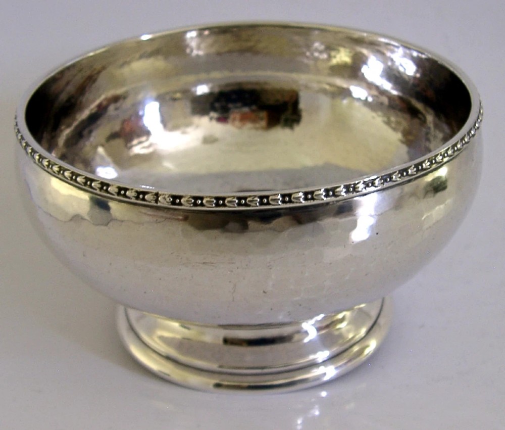 A planished sterling silver bowl featuring a hand-hammered finish, patterned rim, pedestal base, and British hallmarks stamped on the side. View VI