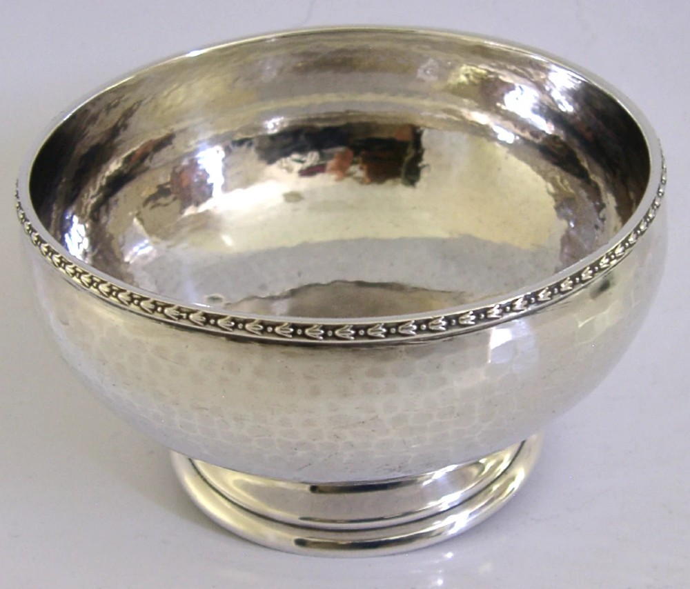 A planished sterling silver bowl featuring a hand-hammered finish, patterned rim, pedestal base, and British hallmarks stamped on the side. View VII