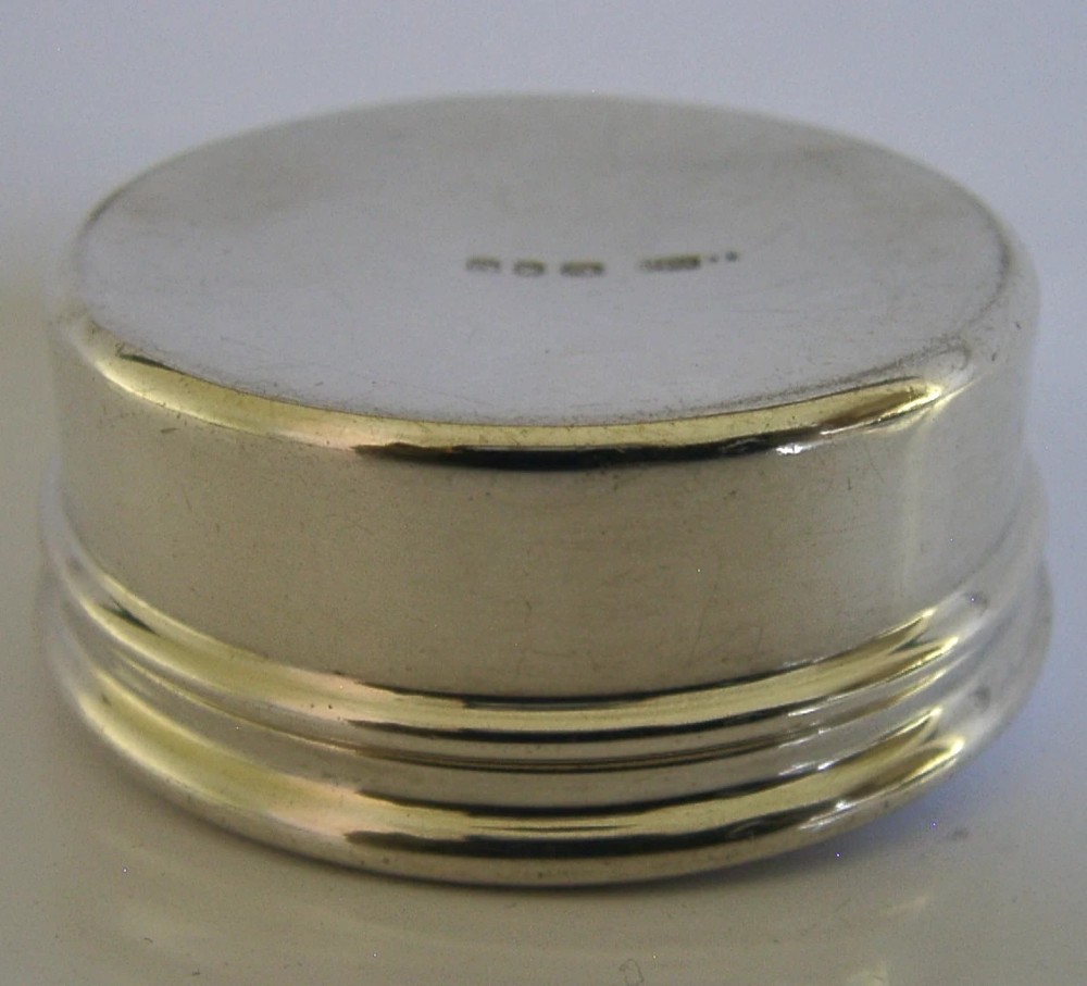 A small circular sterling silver pyx box featuring an engraved cross on the cover and a gold gilt interior. View VI