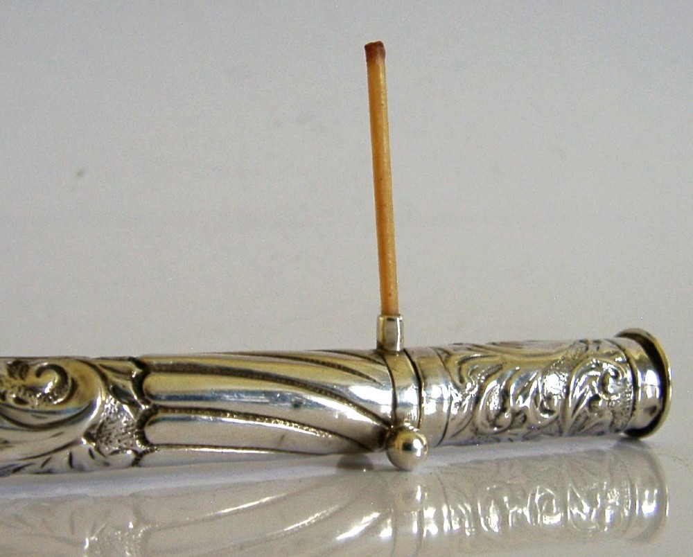 An elongated cylindrical silver Victorian wax holder featuring scrollwork engraving and a camel figure at the terminal. View II