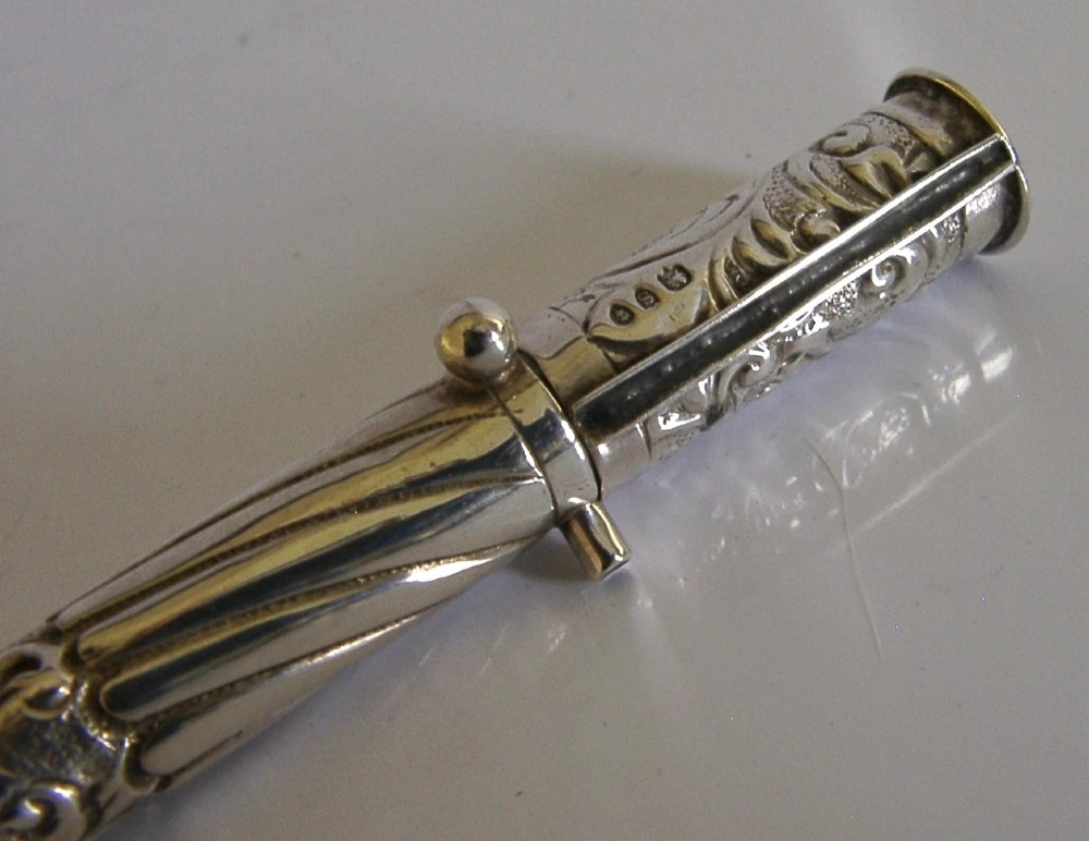 An elongated cylindrical silver Victorian wax holder featuring scrollwork engraving and a camel figure at the terminal. View III