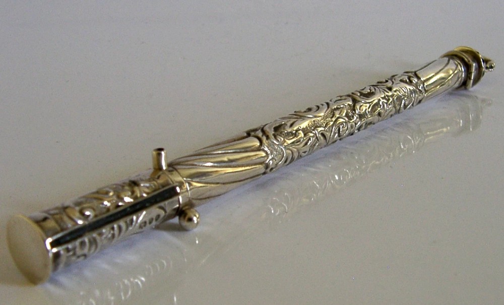 An elongated cylindrical silver Victorian wax holder featuring scrollwork engraving and a camel figure at the terminal. View V