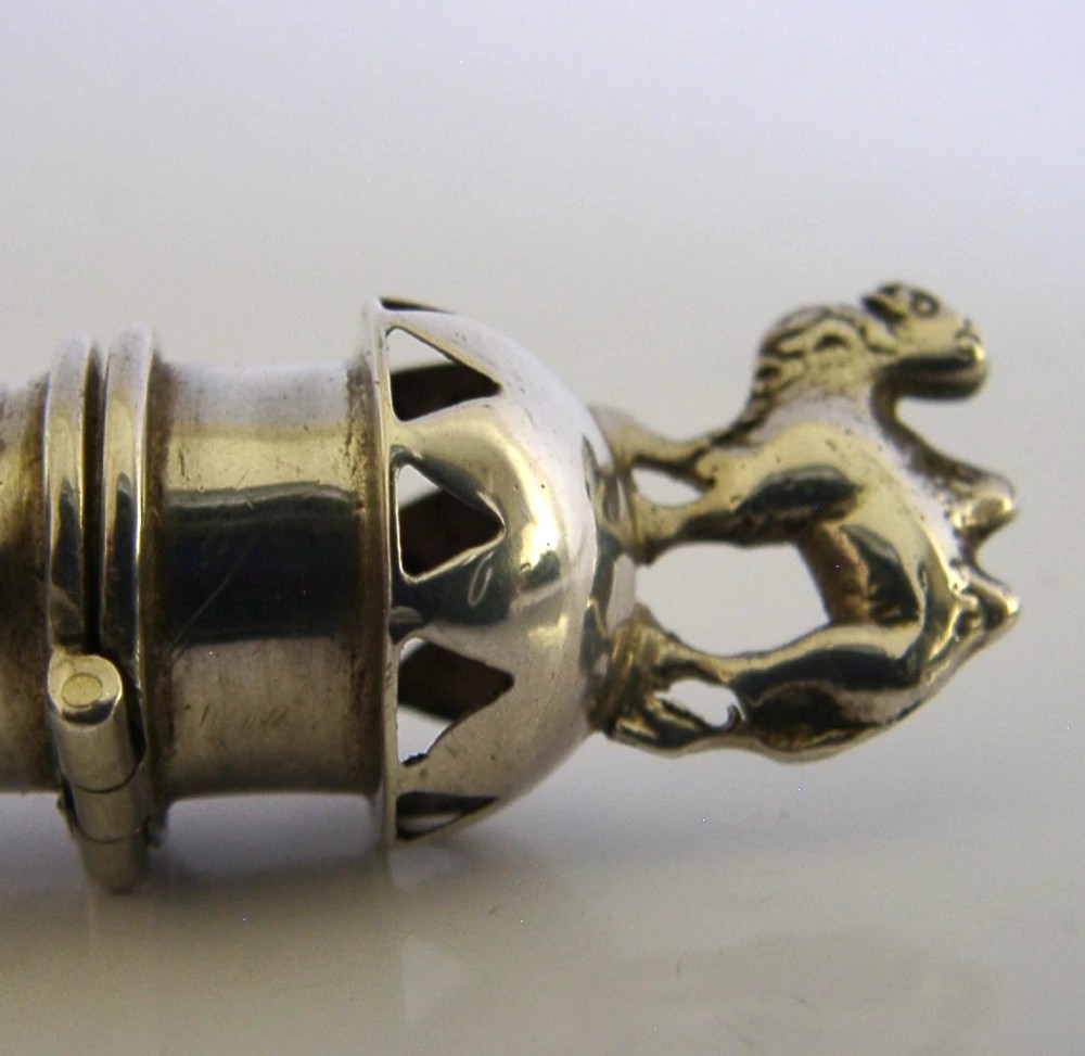 An elongated cylindrical silver Victorian wax holder featuring scrollwork engraving and a camel figure at the terminal. View VII