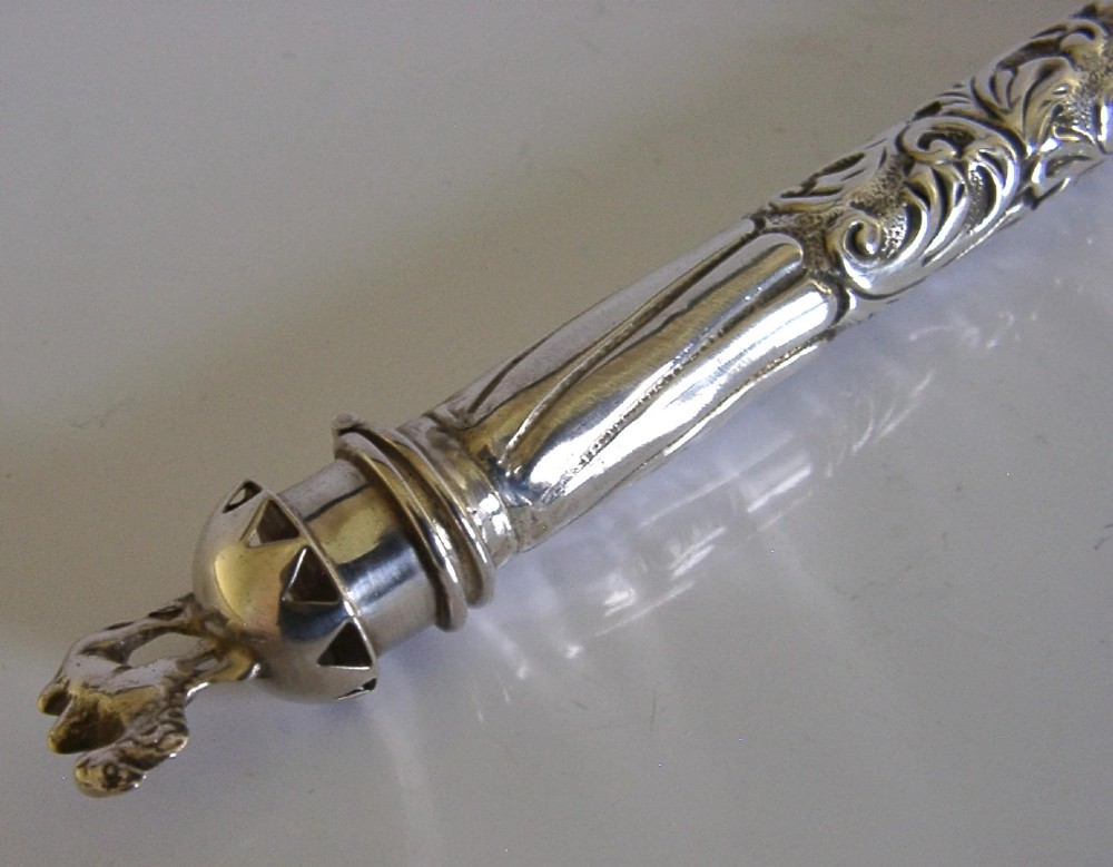 An elongated cylindrical silver Victorian wax holder featuring scrollwork engraving and a camel figure at the terminal. View X
