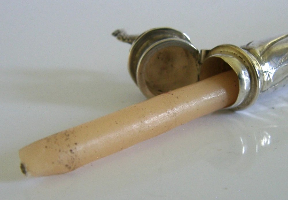 An elongated cylindrical silver Victorian wax holder featuring scrollwork engraving and a camel figure at the terminal. View XII