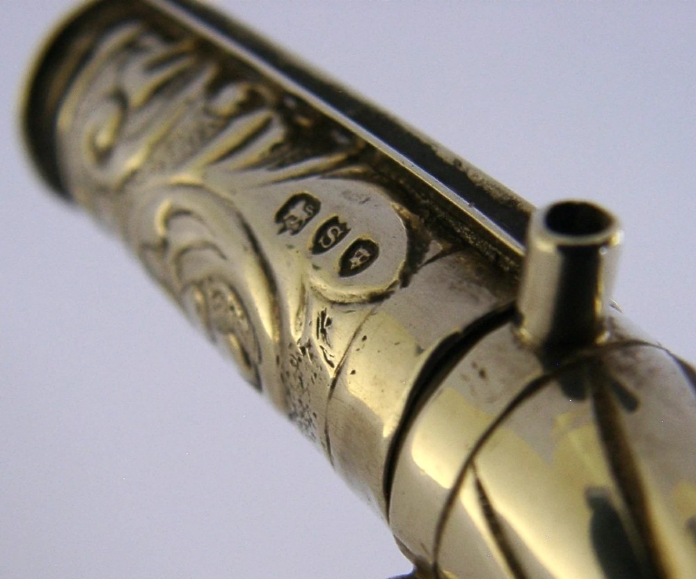 An elongated cylindrical silver Victorian wax holder featuring scrollwork engraving and a camel figure at the terminal. View XIII