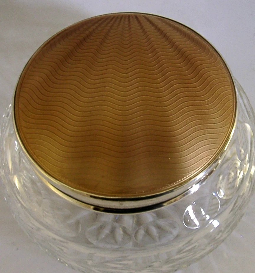 A circular cut glass vanity jar with a sterling silver rim and a bronze guilloche enamelled lid displaying a sunburst pattern. View VII