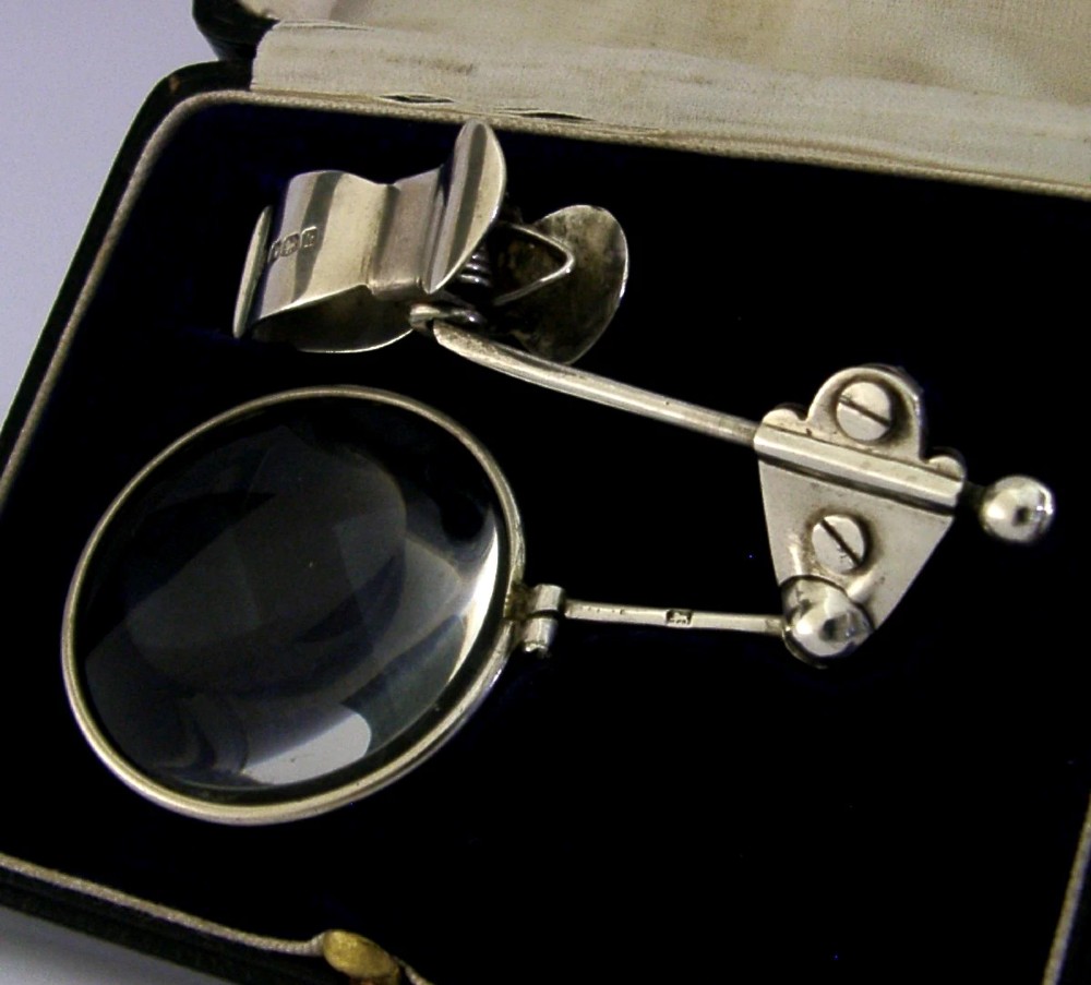 A sterling silver thumb magnifier glass with an adjustable arm clip rested inside a black velvet and silk lined presentation box. View III