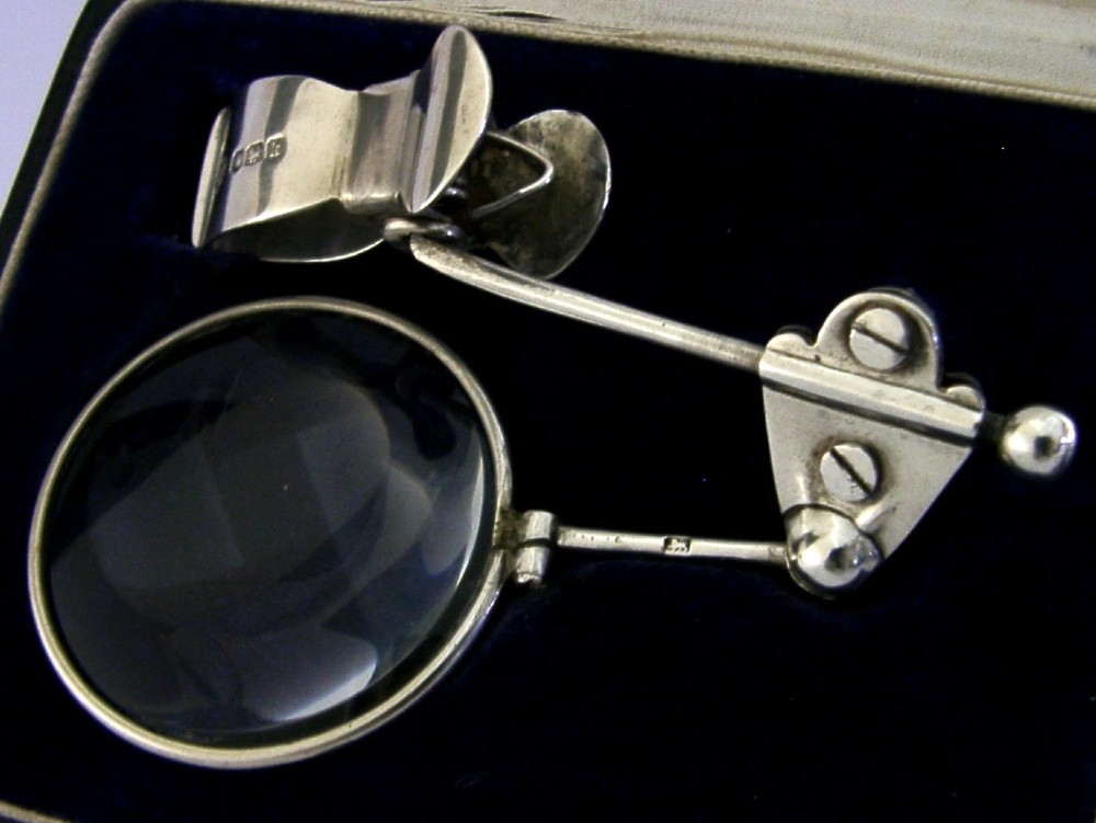 A sterling silver thumb magnifier glass with an adjustable arm clip rested inside a black velvet and silk lined presentation box. View IV