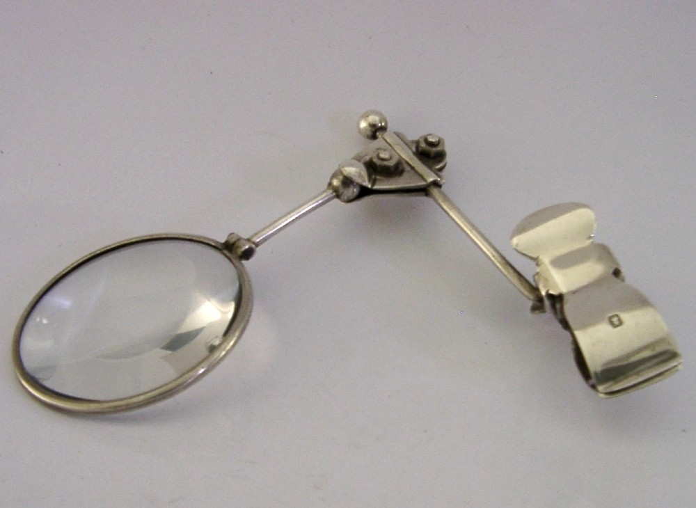 A sterling silver thumb magnifier glass with an adjustable arm clip rested inside a black velvet and silk lined presentation box. View VI