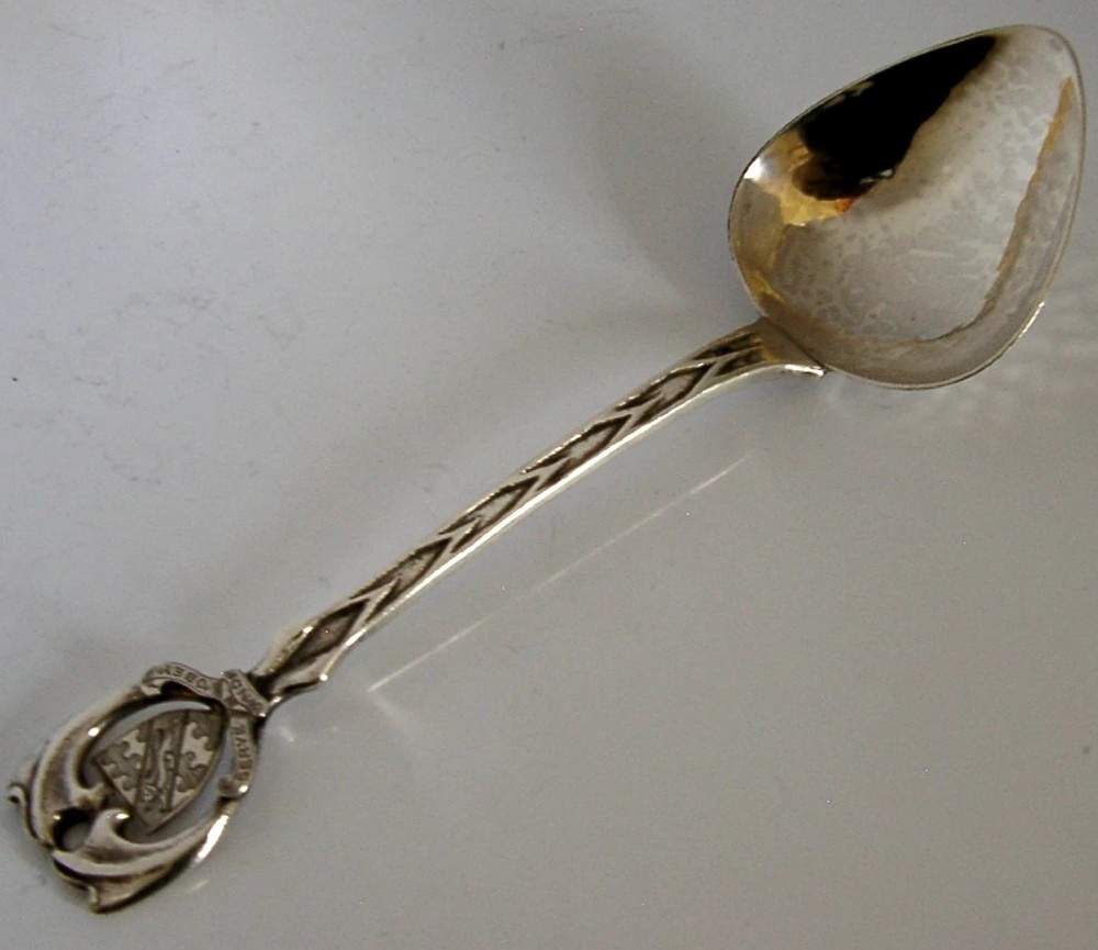 An Art Deco sterling silver spoon featuring an openwork coat of arms handle terminal, a geometric stem, and a polished teardrop bowl.