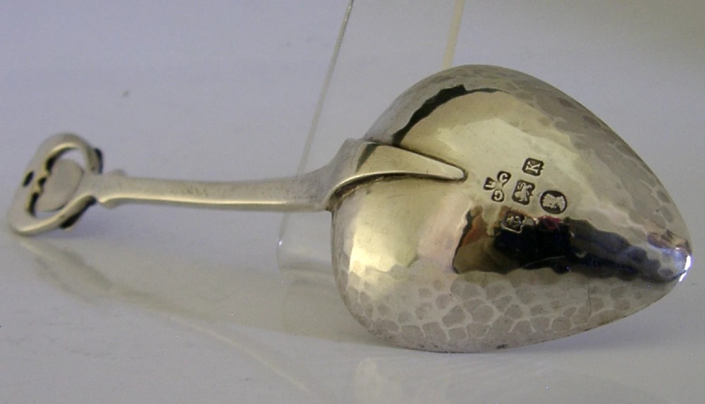 An Art Deco sterling silver spoon featuring an openwork coat of arms handle terminal, a geometric stem, and a polished teardrop bowl. View V