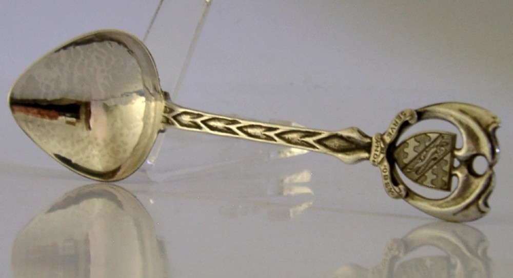 An Art Deco sterling silver spoon featuring an openwork coat of arms handle terminal, a geometric stem, and a polished teardrop bowl. View VII