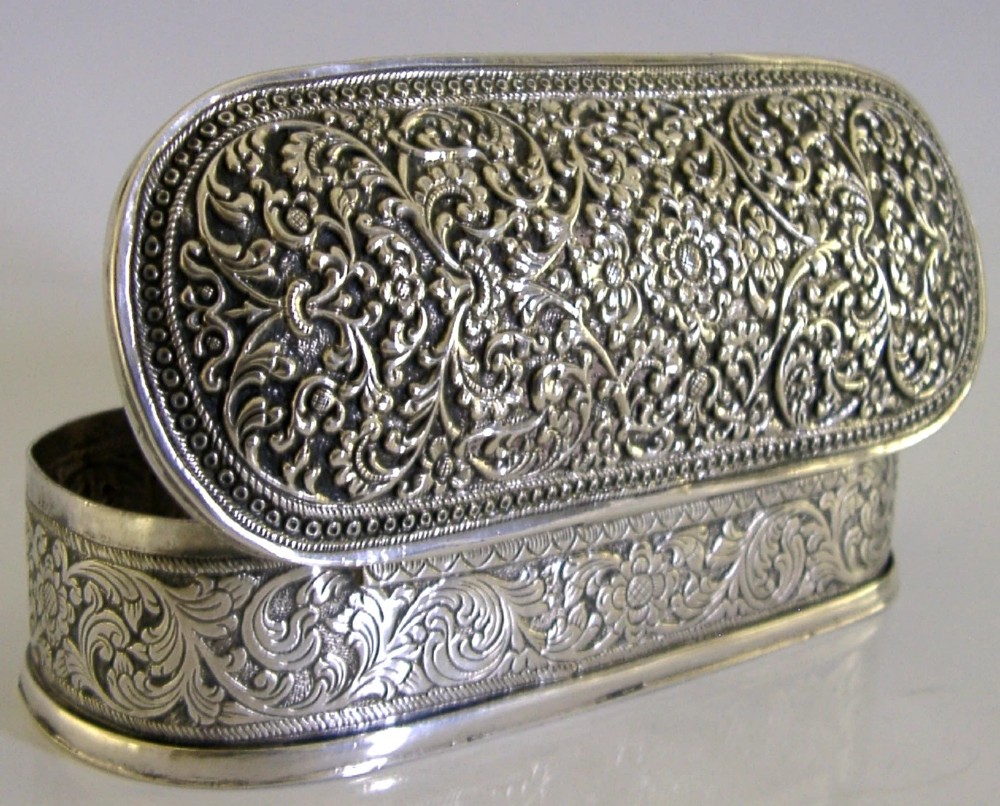 An oval antique solid silver box decorated with elaborate hand-chased floral repousse scrollwork.