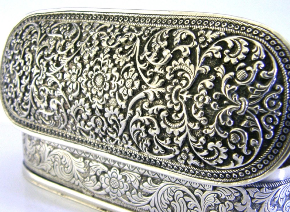 An oval antique solid silver box decorated with elaborate hand-chased floral repousse scrollwork. View II