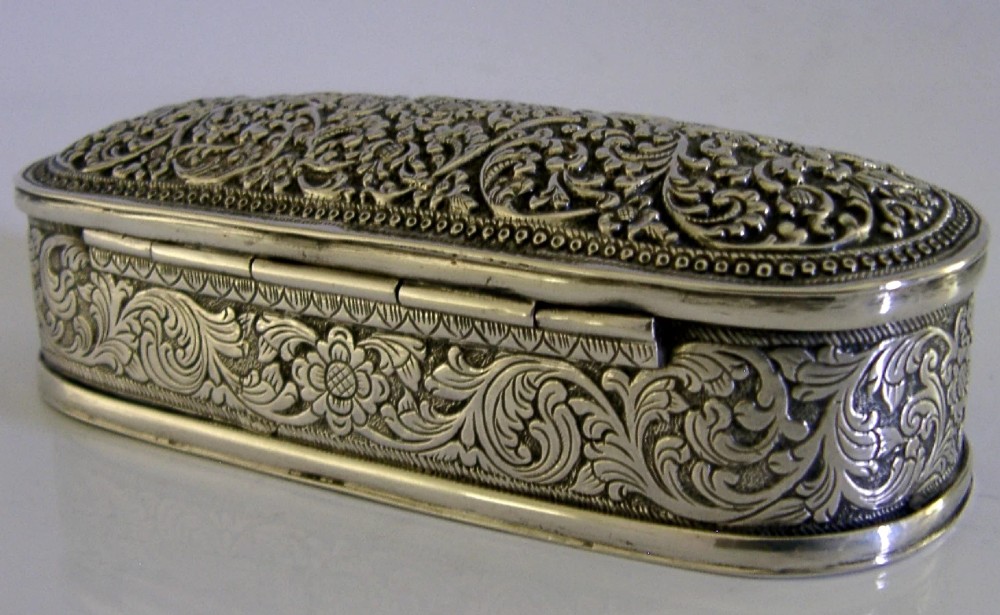An oval antique solid silver box decorated with elaborate hand-chased floral repousse scrollwork. View V