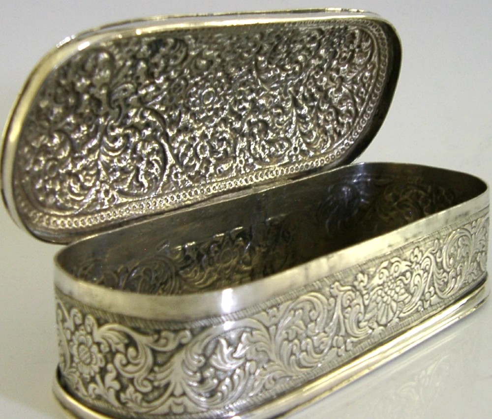 An oval antique solid silver box decorated with elaborate hand-chased floral repousse scrollwork. View VII