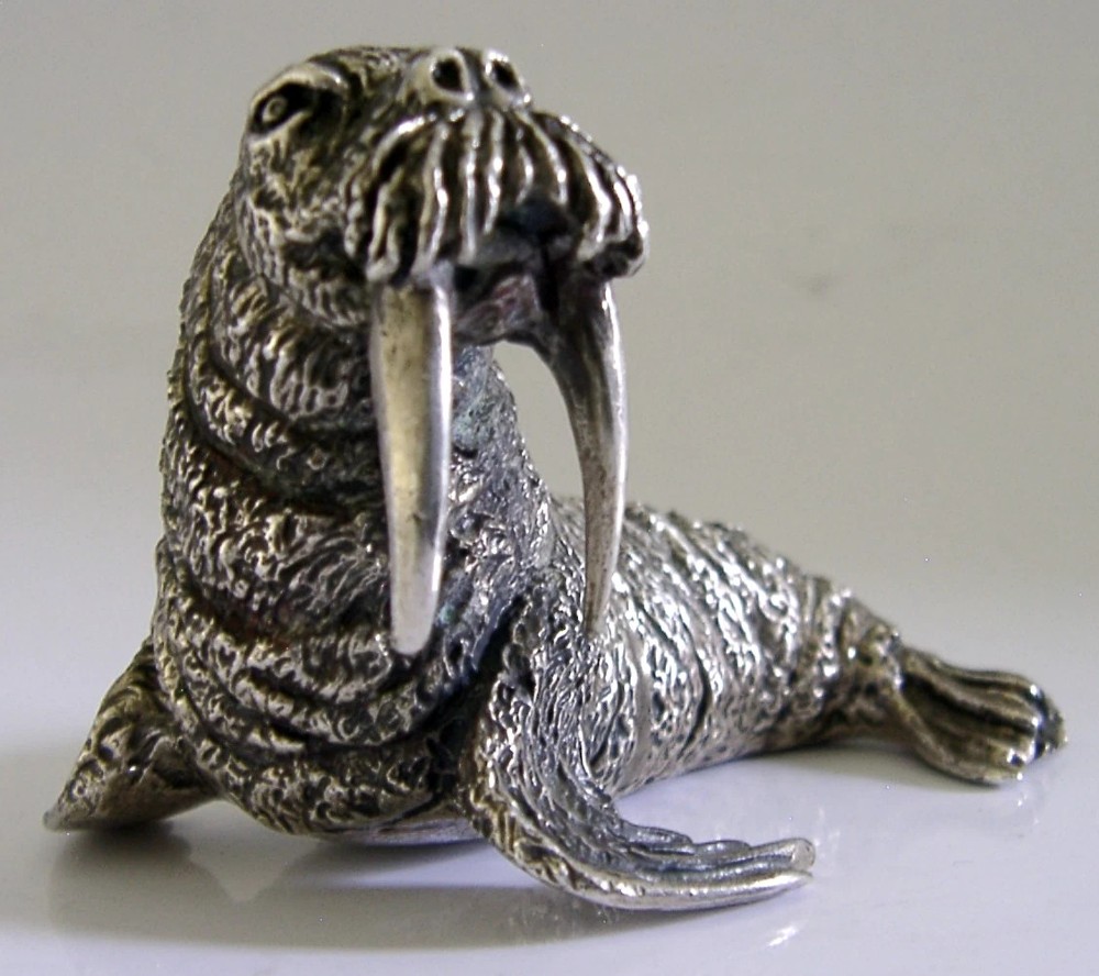 A detailed cast silver walrus figurine shown in profile with long downward tusks and textured skin. View II