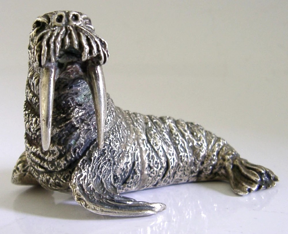 A detailed cast silver walrus figurine shown in profile with long downward tusks and textured skin. View III