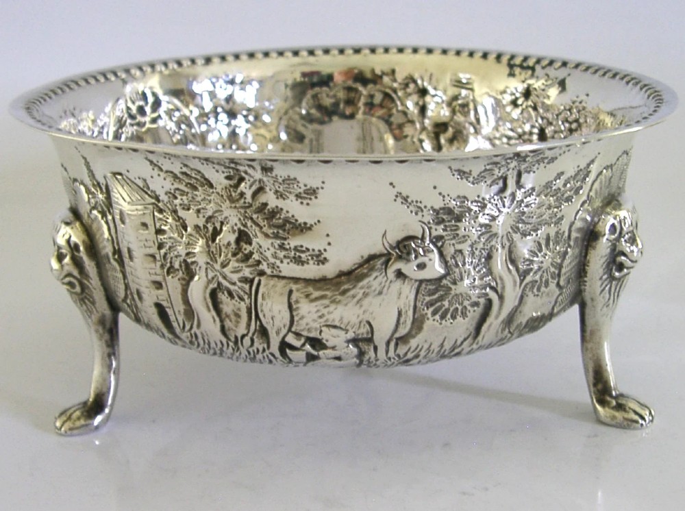 A late Victorian sterling silver bowl decorated with chased pastoral scenes and supported by three lion-mask legs.