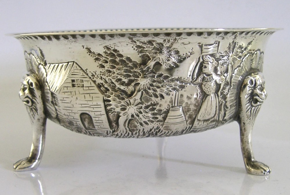 A late Victorian sterling silver bowl decorated with chased pastoral scenes and supported by three lion-mask legs. View II