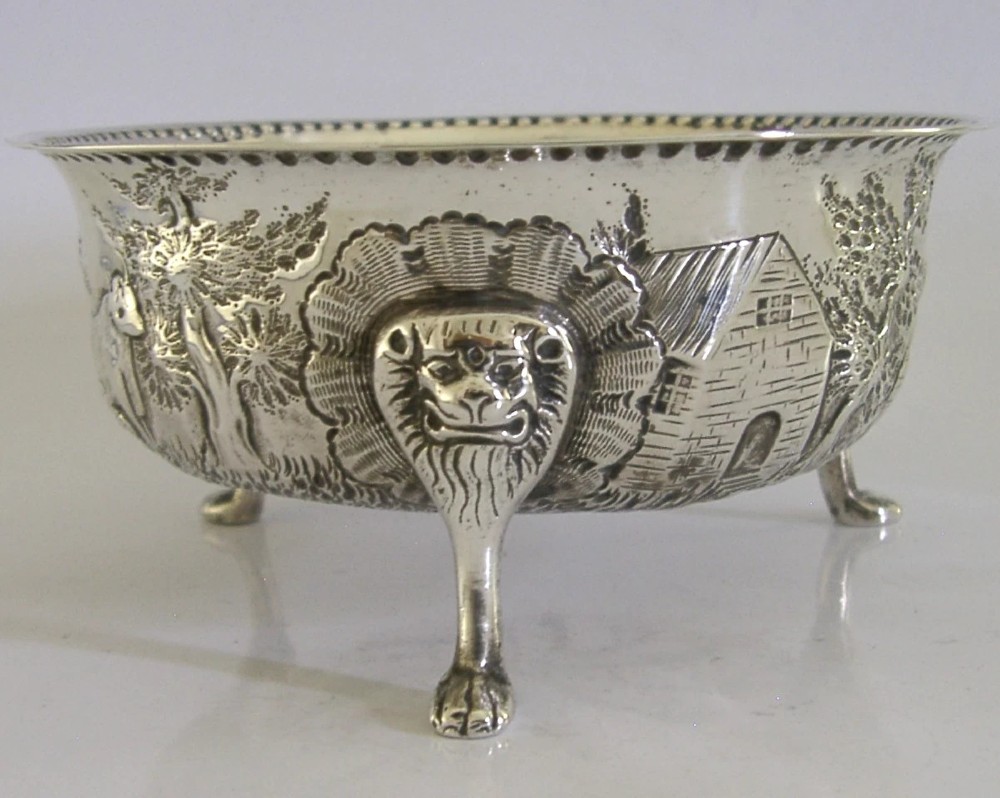 A late Victorian sterling silver bowl decorated with chased pastoral scenes and supported by three lion-mask legs. View IV