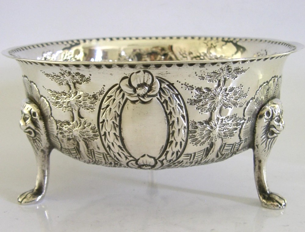 A late Victorian sterling silver bowl decorated with chased pastoral scenes and supported by three lion-mask legs. View V